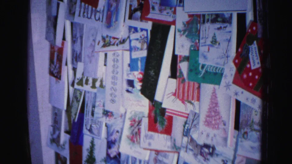 Christmas greeting card wall display, 8mm home movie circa 1962 Hagerstown Maryland; Noel, Glad, and Christmas tree cards in a layered arrangement.