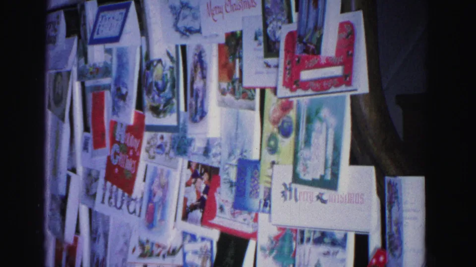 Close view of wall-mounted Christmas cards with holiday illustrations and readable text in a domestic interior, Hagerstown Maryland circa 1962
