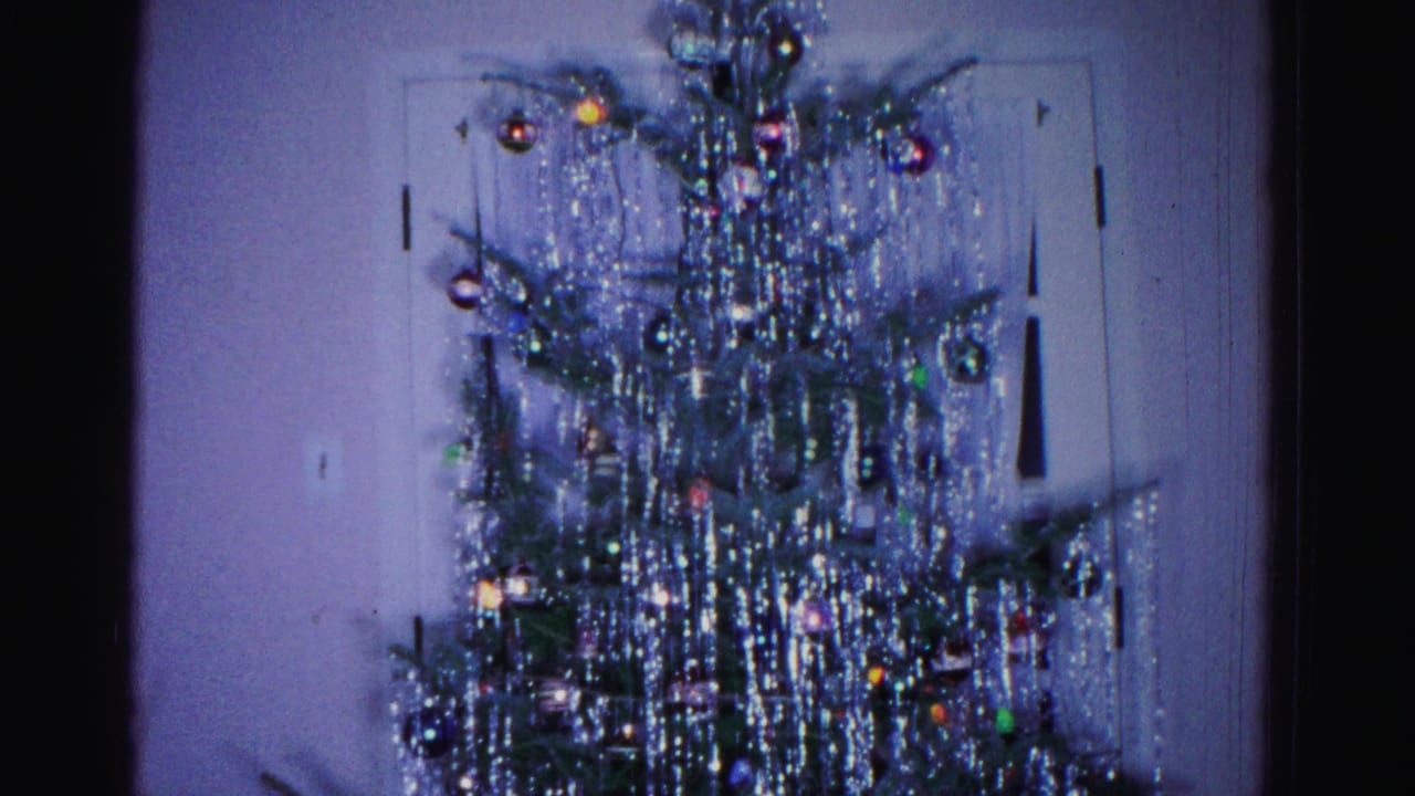 Mid-section of tinsel-covered Christmas tree with colorful ornaments, white paneled door visible in background.