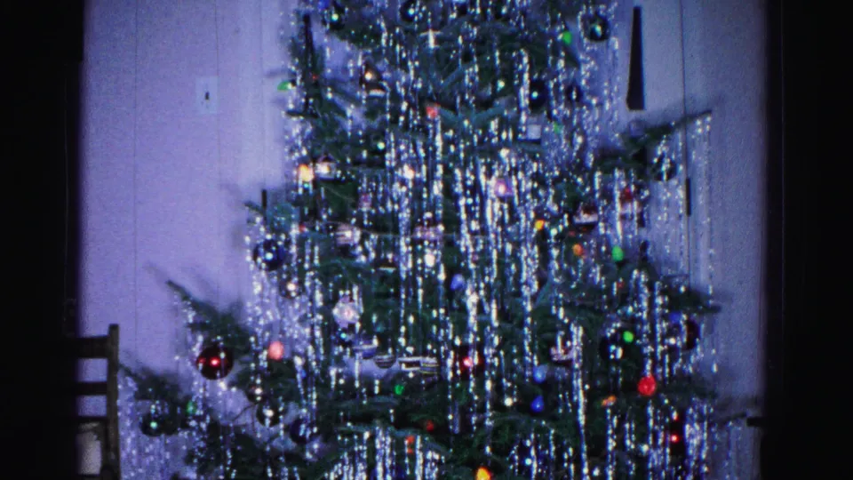 Base and stand of a decorated Christmas tree on 8mm film, with heavy silver tinsel and a wooden chair in a domestic interior, circa 1962.