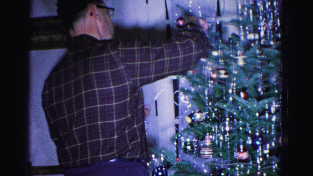 Man in plaid shirt decorating a tinsel-draped Christmas tree with colored glass ornaments, 8mm home movie, Hagerstown, Maryland, 1962.