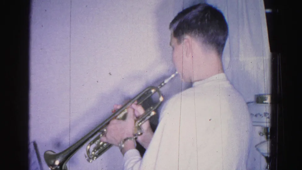 Young person in white shirt playing trumpet, slight profile visible, 8mm home movie interior, Hagerstown, Maryland, circa 1962.