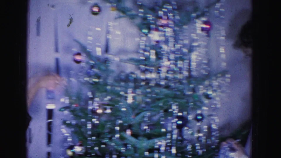 Two adults decorate a Christmas tree with round glass ornaments and silver tinsel in what appears to be a 1962 home interior, Hagerstown, Maryland.