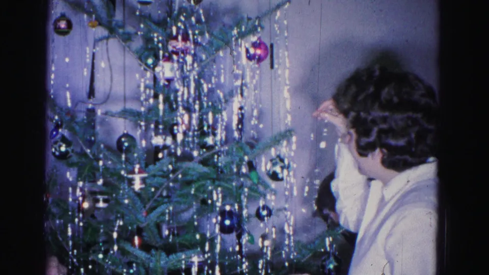 An adult leans in while decorating a Christmas tree with glass ornaments and dense silver tinsel in what appears to be a 1962 domestic interior, Hagerstown, Maryland.