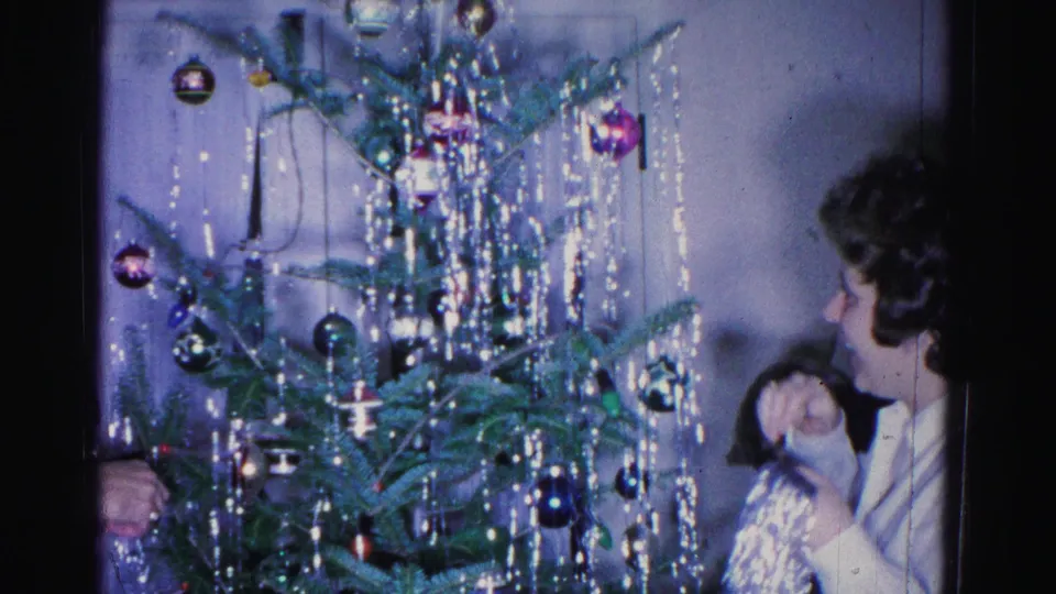 Two adults stand beside a decorated Christmas tree in what appears to be a 1962 residential interior, Hagerstown, Maryland, with glass ball ornaments and dense silver tinsel visible.