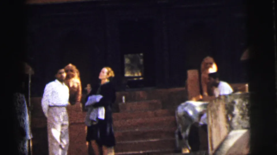 Man in white shirt and woman in dark dress at a Hindu temple entrance, a pale cow visible on stone steps, Calcutta, India, circa 1962, 8mm home movie.