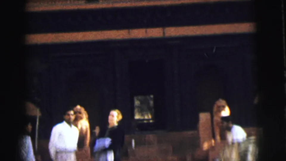 Three people near the entrance of a Hindu temple, including a man in white and a woman in dark dress, Calcutta, India, circa 1962, 8mm home movie.