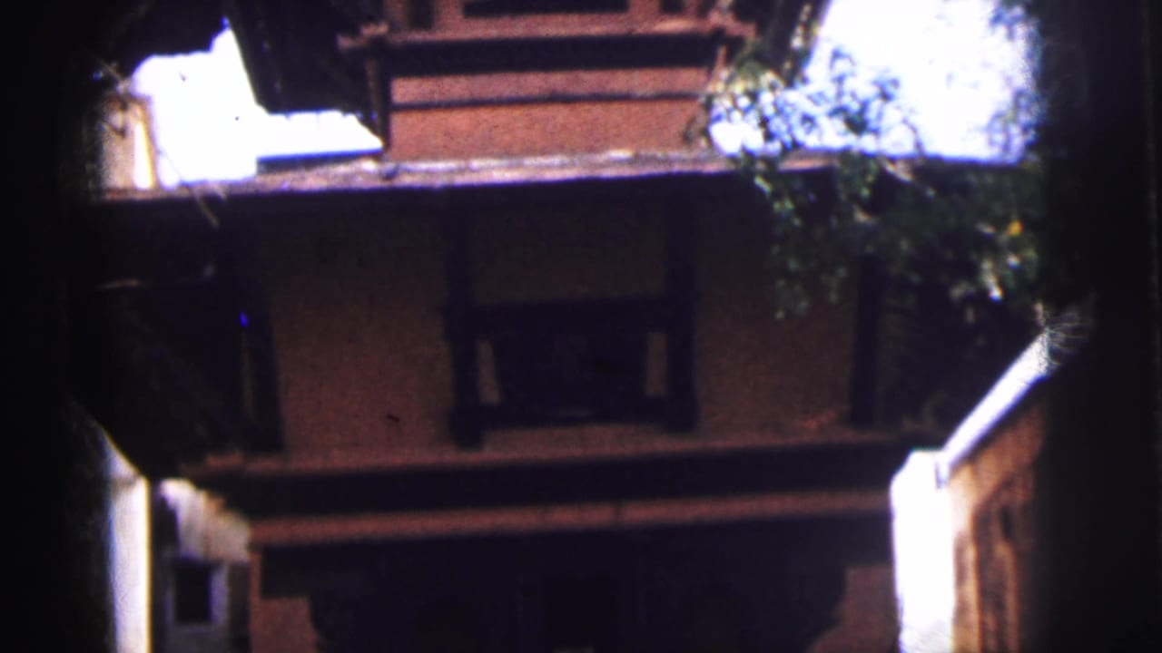 Upward-angled view of a multi-tiered reddish-brown brick building with decorative cornices, partially framed by trees.