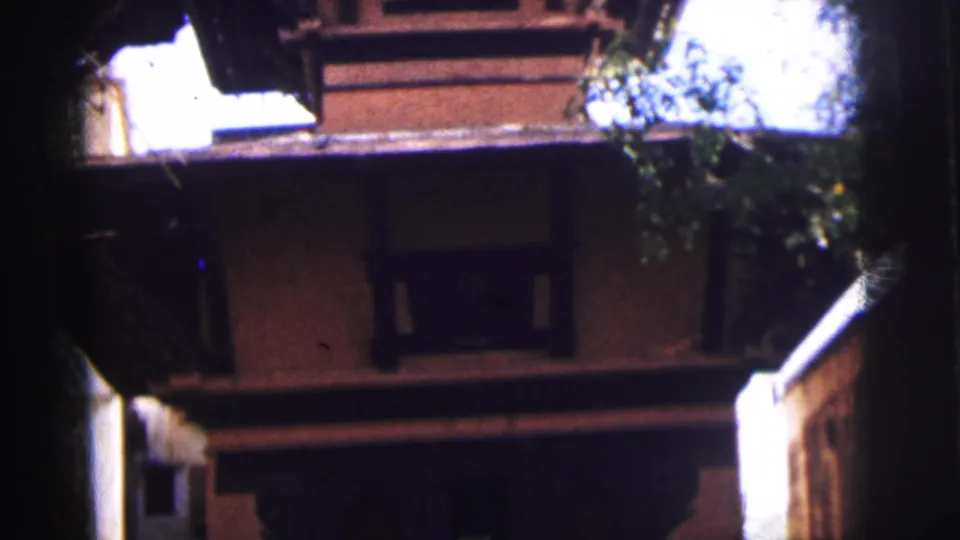8mm home-movie frame showing a multi-storey religious building in Calcutta, India, circa 1962, filmed from below with tree foliage at the top edge.