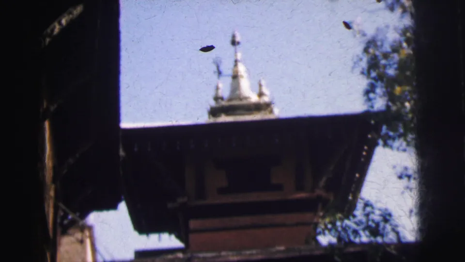 8mm home-movie frame, Calcutta India circa 1962, showing white spire finials at the top of a tiered religious structure with a bird visible in flight against open sky.