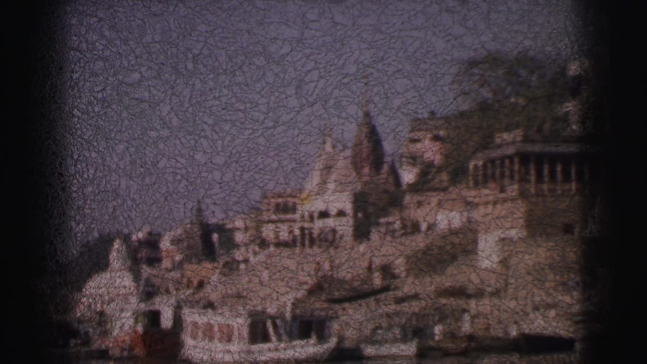 8mm pan shot, circa 1962, of clustered Hindu temple shikhara towers and tiered stone ghat buildings rising from an Indian riverbank.