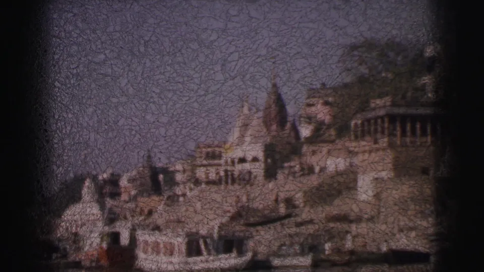 8mm pan shot, circa 1962, of clustered Hindu temple shikhara towers and tiered stone ghat buildings rising from an Indian riverbank.