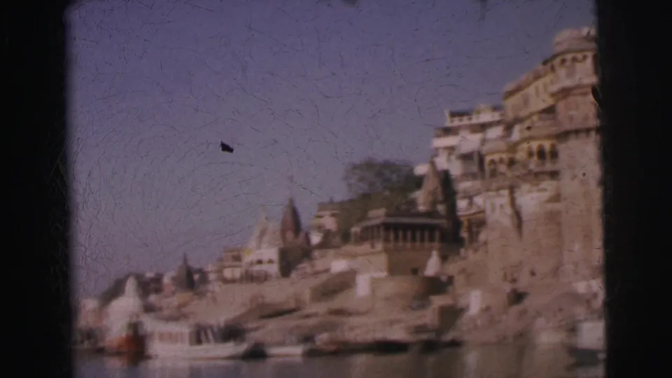 Continuing 8mm pan, circa 1962, showing stepped stone ghats, curved temple shikhara towers, and multi-story palatial buildings along an Indian riverfront.