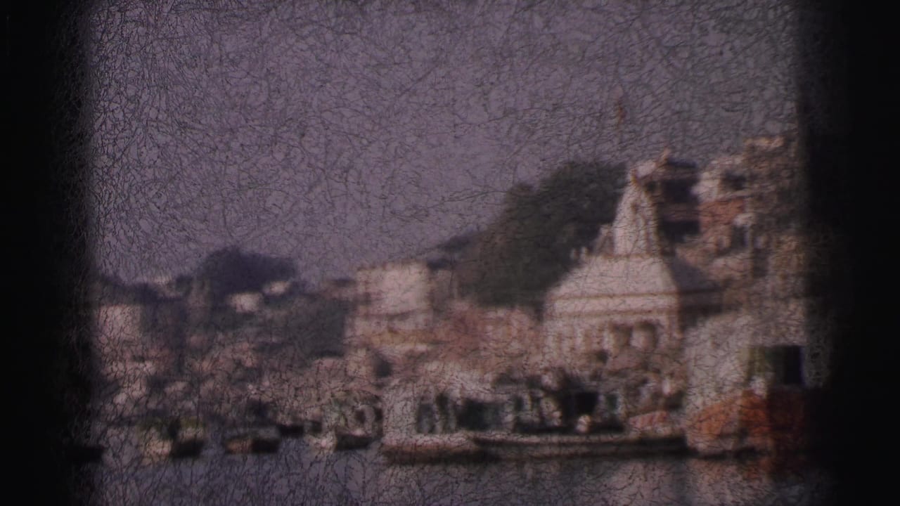 Riverfront view with a prominent white temple dome at centre, buildings to either side, wooden boats along the bank, emulsion crackle across the frame.