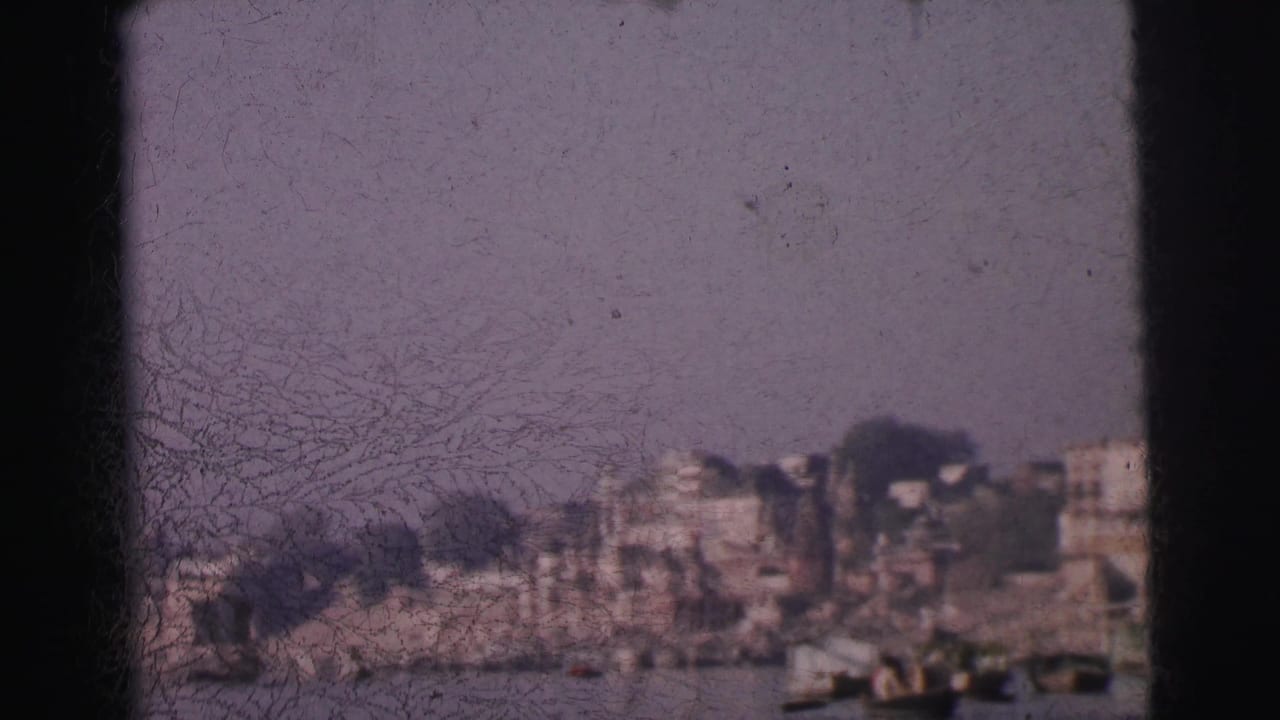 8mm home-movie frame circa 1962 showing a row of multi-storey buildings lining a wide river in Calcutta, India, with small boats and heavy film deterioration.