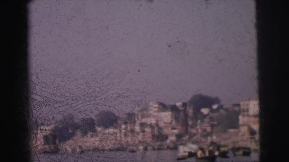 8mm home-movie frame circa 1962 showing a row of multi-storey buildings lining a wide river in Calcutta, India, with small boats and heavy film deterioration.