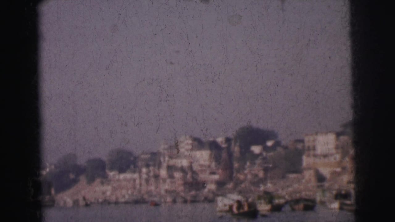 8mm view of the same riverbank skyline showing multi-storey buildings and moored boats; film-gate border visible at right edge.