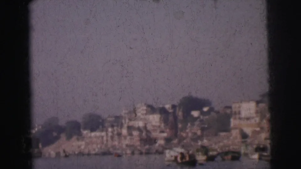 8mm home-movie frame circa 1962 showing Calcutta's far riverbank with closely packed multi-storey buildings, small boats, and a pale hazy sky.