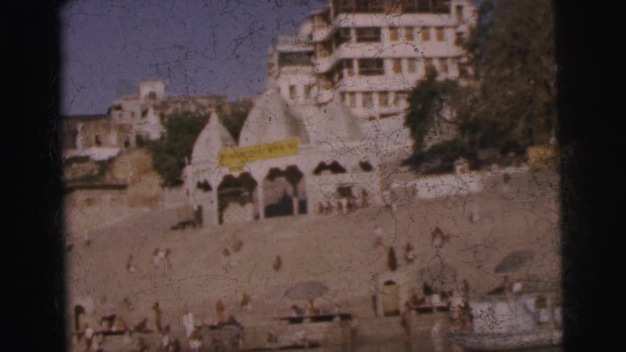 Calcutta riverfront ghat, 1962 — stepped embankment with temple spire, multi-story whitewashed building bearing a yellow banner, and scattered figures on the steps