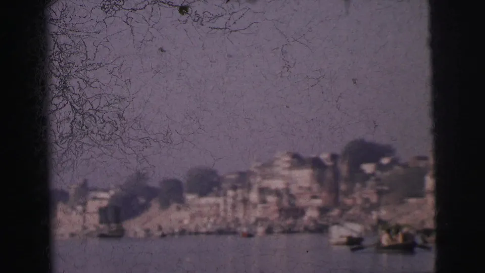 Calcutta riverfront from midstream, 1962 — city buildings line the far bank; bare tree branches frame the upper left; emulsion scratches cross the frame