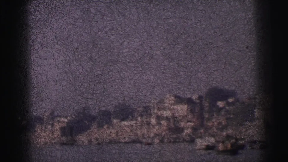 Calcutta riverfront panorama, 1962 — pale buildings along the far bank viewed from water; frame shows significant emulsion damage typical of aged 8mm stock