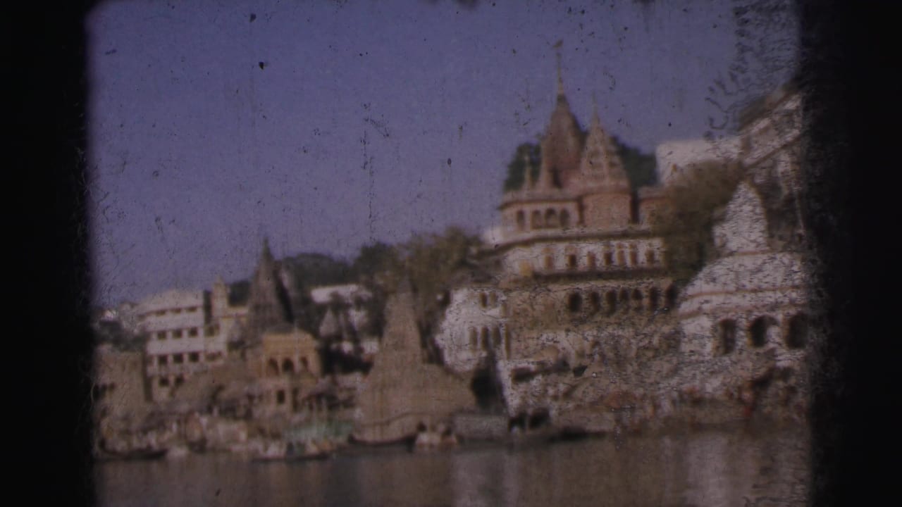 Riverside view of Indian temple complex and ornate multi-story building above ghats, 8mm film, c.1962.