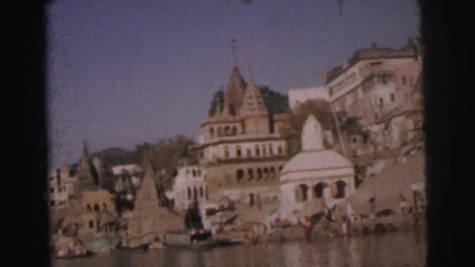 Multi-spired Hindu temples, white dome, and ghat steps at river's edge with figures visible, Calcutta, India, 1962, 8mm film.