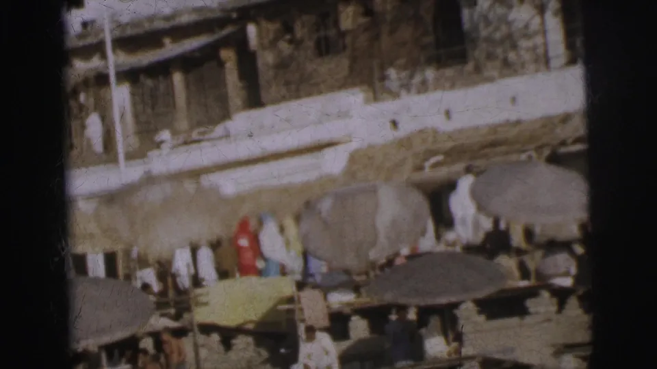 Tiered ghat steps with worshippers and vendors under canopies, upper building facade more visible, Calcutta, circa 1962.