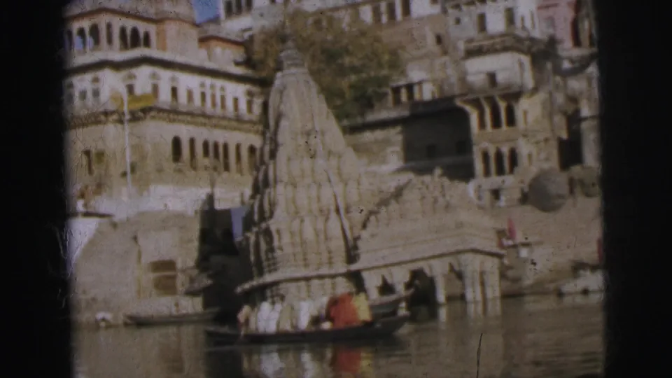 Shikhara-style temple towers and arcaded riverside buildings viewed from the river, with a small wooden boat carrying figures, Calcutta, circa 1962.