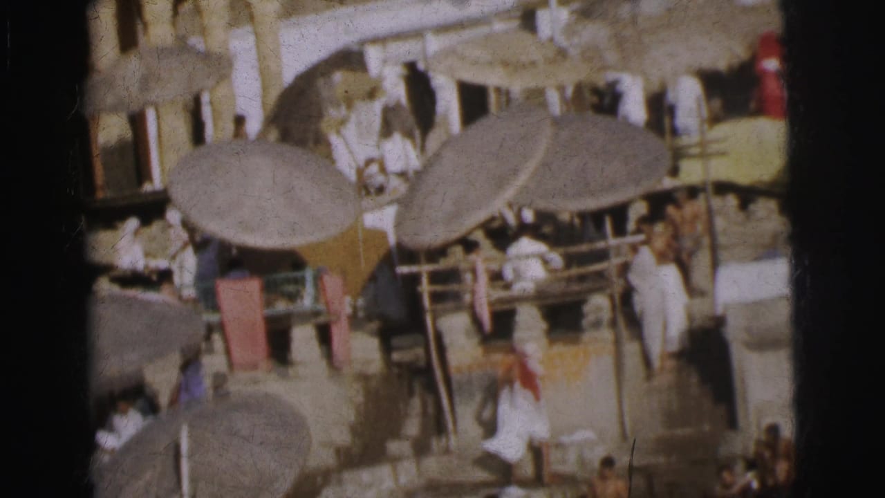 Elevated view of a marketplace with thatched parasols, wooden railing, and figures in traditional white dress.