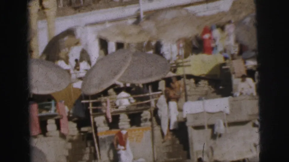 Overhead 8mm shot of Calcutta market stalls circa 1962, showing thatched parasols, white-robed figures, red fabric, and a yellow cloth spread.