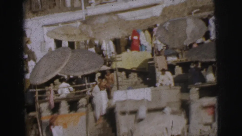 8mm color footage of Calcutta open-air market circa 1962, showing thatched-parasol stalls, white-clad pedestrians, and spread yellow goods or cloth.