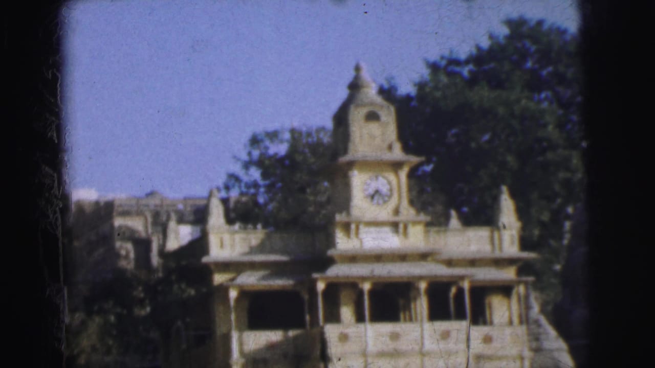 Clock tower with colonnaded balconies against blue sky, filmed on 8mm.