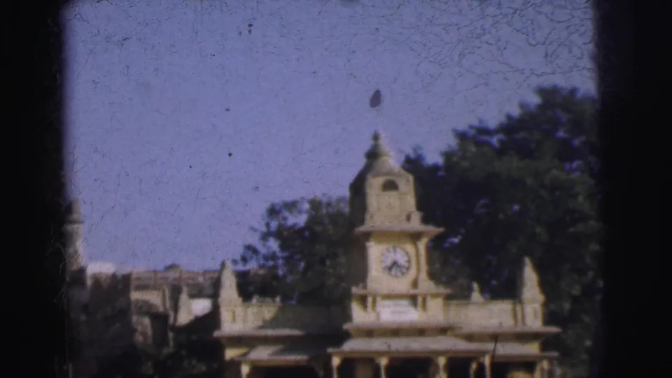 Standalone clock tower pavilion at riverside with trees and blue sky, Calcutta, India, circa 1962, 8mm color film.