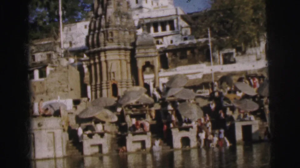 Crowded stone river ghat with temple pavilions, people wading and gathered on steps, Calcutta, India, circa 1962, 8mm color film.