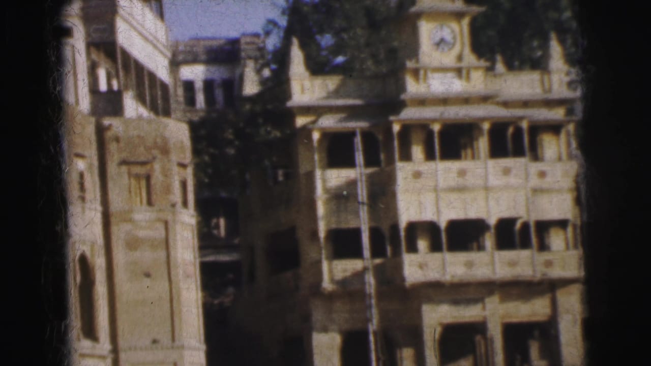 Ornate multi-story building with clock tower at upper right, arched balconies, and weathered stucco facade on aged 8mm film.