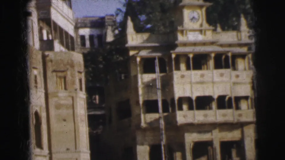 Calcutta colonial-era building complex with clock tower, arched balconies, and pale stucco, circa 1962, on color 8mm with visible warm color fading.