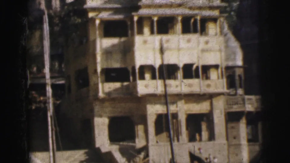 Lower section of ornate colonial-era buildings in Calcutta, circa 1962, showing arched balcony rows, a wooden utility pole, and flanking foliage on aged 8mm film.