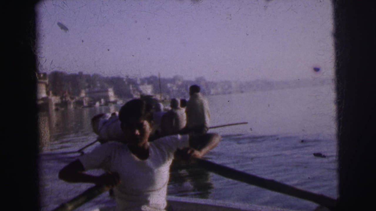 A young man rows a wooden boat on the river at Calcutta, circa 1962, with passengers behind him and a hazy distant cityscape along the far bank.