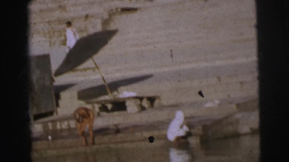 Ghat steps with a small shelter structure and parasol; adults in white garments and a partially undressed figure near the waterline, circa 1962 Calcutta.