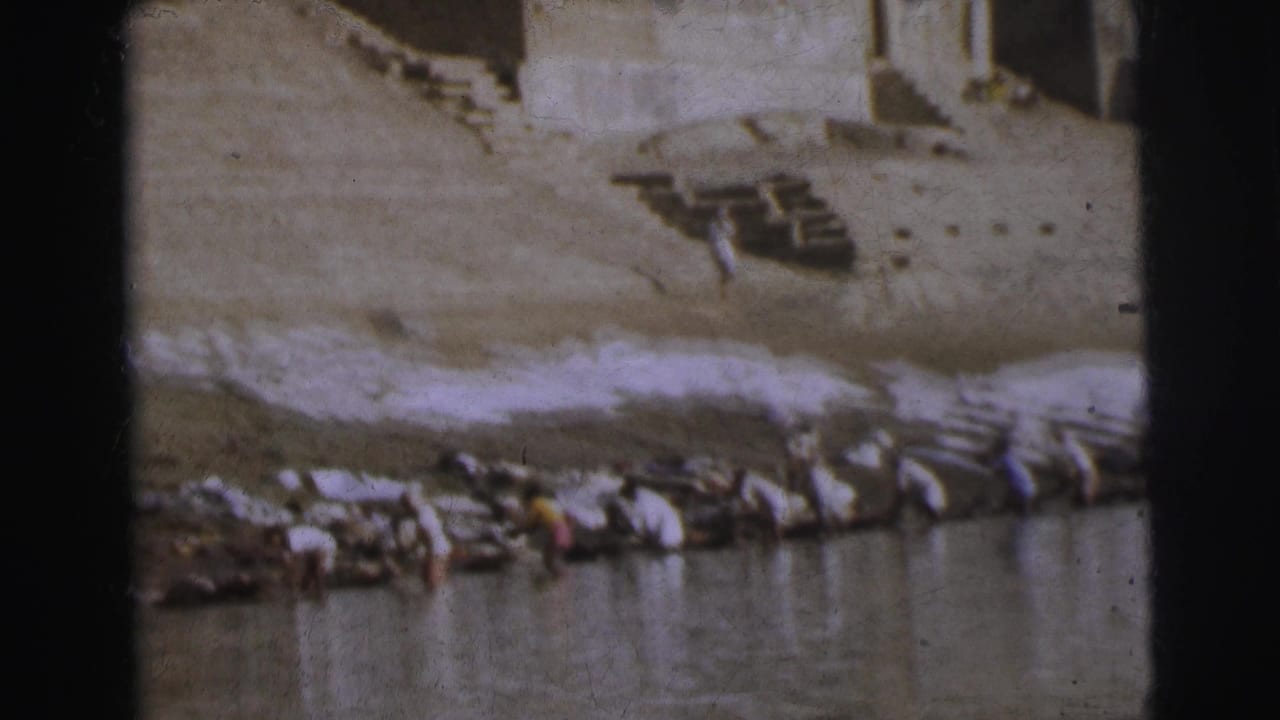 Row of figures crouched along stone ghat steps with white laundry spread across the bank.