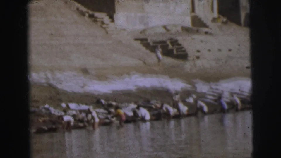 8mm footage of figures washing laundry along stone ghat steps in Calcutta, 1962, with white fabric spread prominently across the bank.
