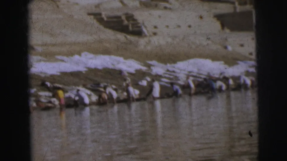 8mm frame of people washing and laying out laundry on the stone ghat bank, Calcutta, 1962, with figures reflected in the water below.