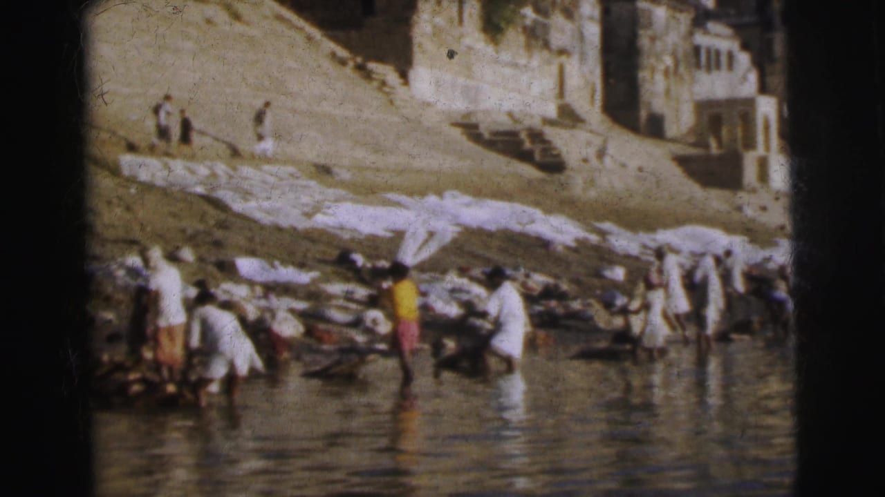 Mid-distance view of washers at a Calcutta river ghat, 1962 — figures in white and colored dress work at the waterline with cloth laid flat on the steps and terraced buildings visible above.