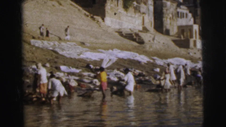 Mid-distance view of washers at a Calcutta river ghat, 1962 — figures in white and colored dress work at the waterline with cloth laid flat on the steps and terraced buildings visible above.