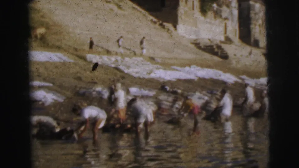 Closer view of washers at the ghat bank, Calcutta, 1962 — figures stoop at the waterline while white fabrics dry on the steps and birds pass overhead.