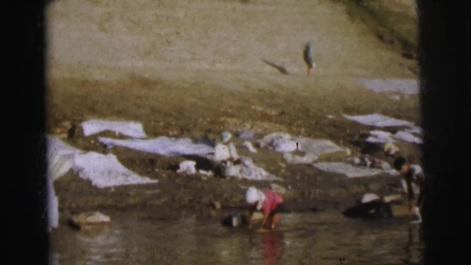 Close view of washers at the ghat bank, Calcutta, 1962 — three or four figures bent over stones scrubbing laundry, with white cloths on steps and one person in a pink garment visible.