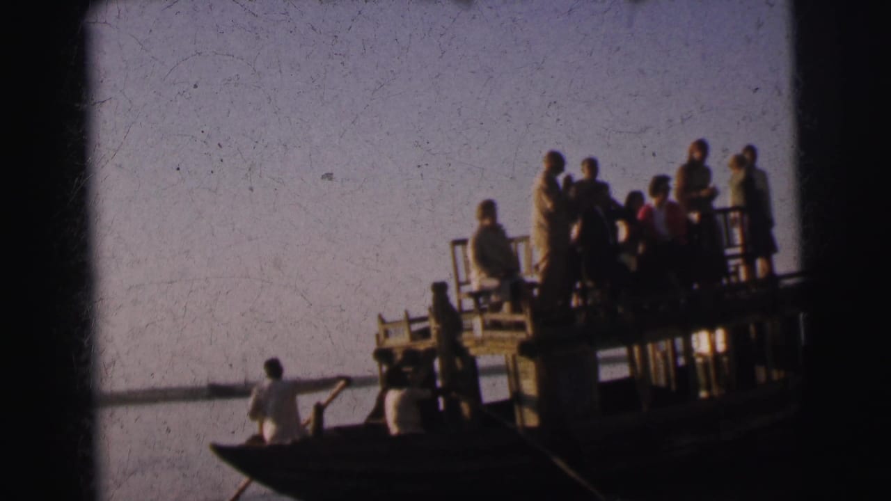 Group on the platform barge with the rowboat and oarsman alongside; figures stand against an open pale sky.