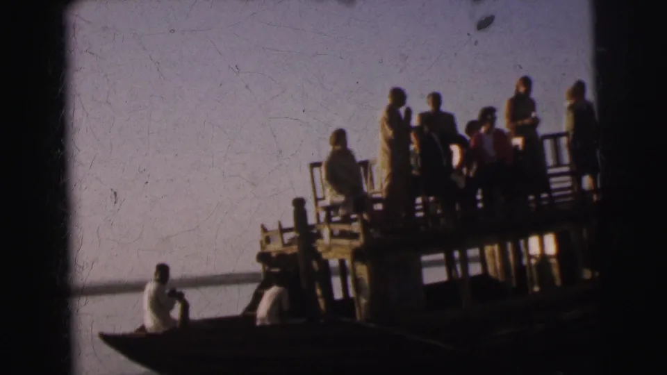 Slightly lower angle reveals the wooden post-and-beam structure beneath the river platform with the group above and an oarsman alongside, circa 1962 Calcutta, India.