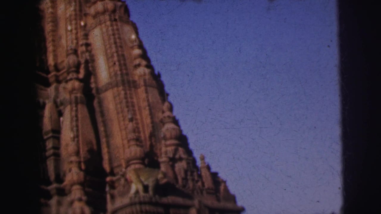 Monkey perched on carved stone ledge of ornate temple shikhara, shot from below against blue sky.